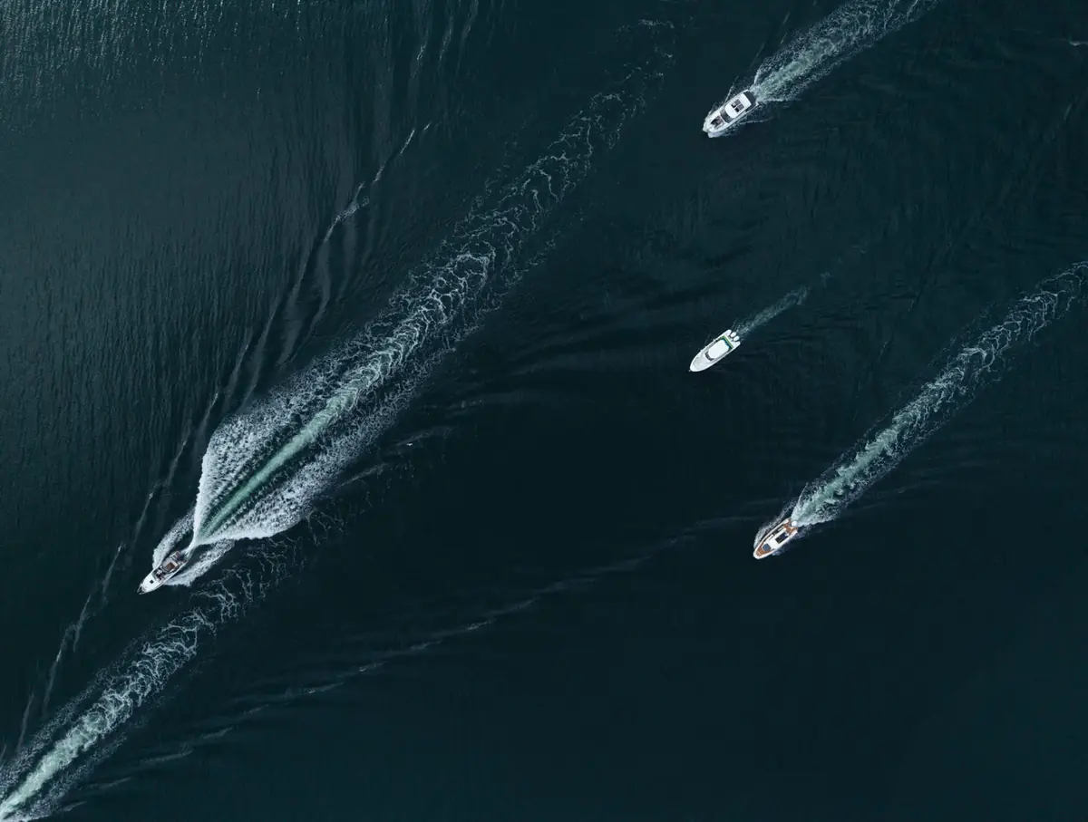 Four motorboats running in formation across dark water, seen from above